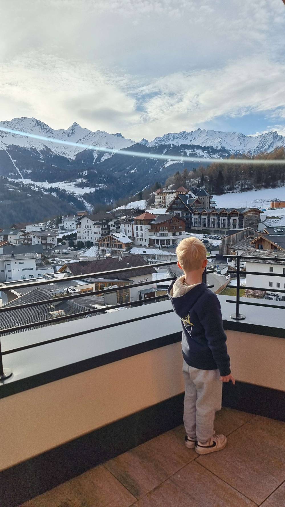 A child stands on a balcony overlooking a mountain village.