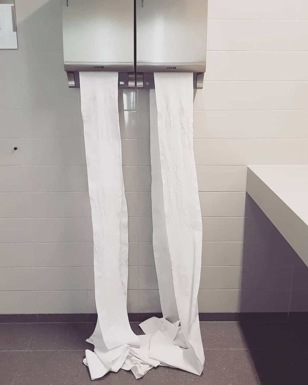 Toilet paper unspooled and draped from wall-mounted dispensers in a bathroom.