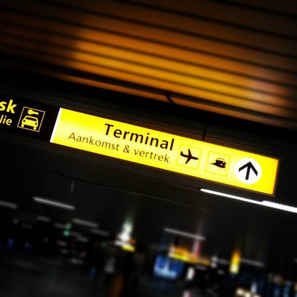 A backlit airport sign reading 'Terminal, Aankomst & vertrek' with directional arrows.