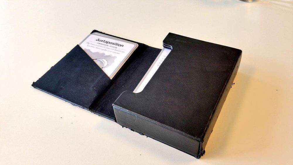 A black card game box with a card reading "Juxtaposition" propped against it on a table.