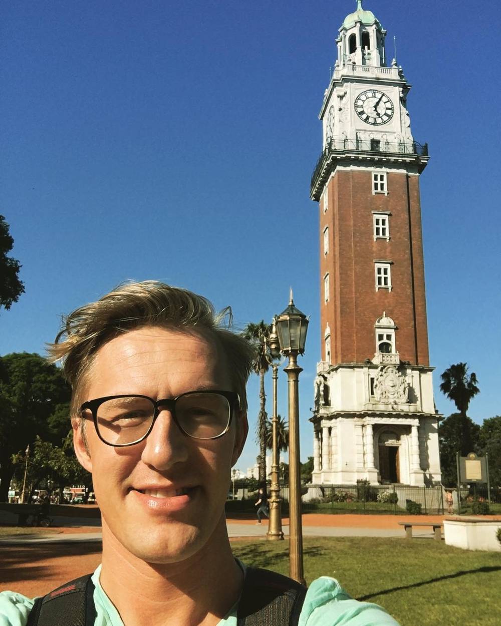 A selfie of a smiling man in glasses in front of the Torre Monumental clock tower in Buenos Aires.