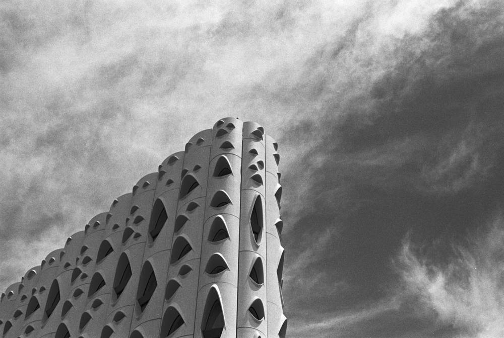 Low angle view of the Populus Hotel, its white facade covered in repeating eyelid shaped window pods rising into a partly cloudy sky.