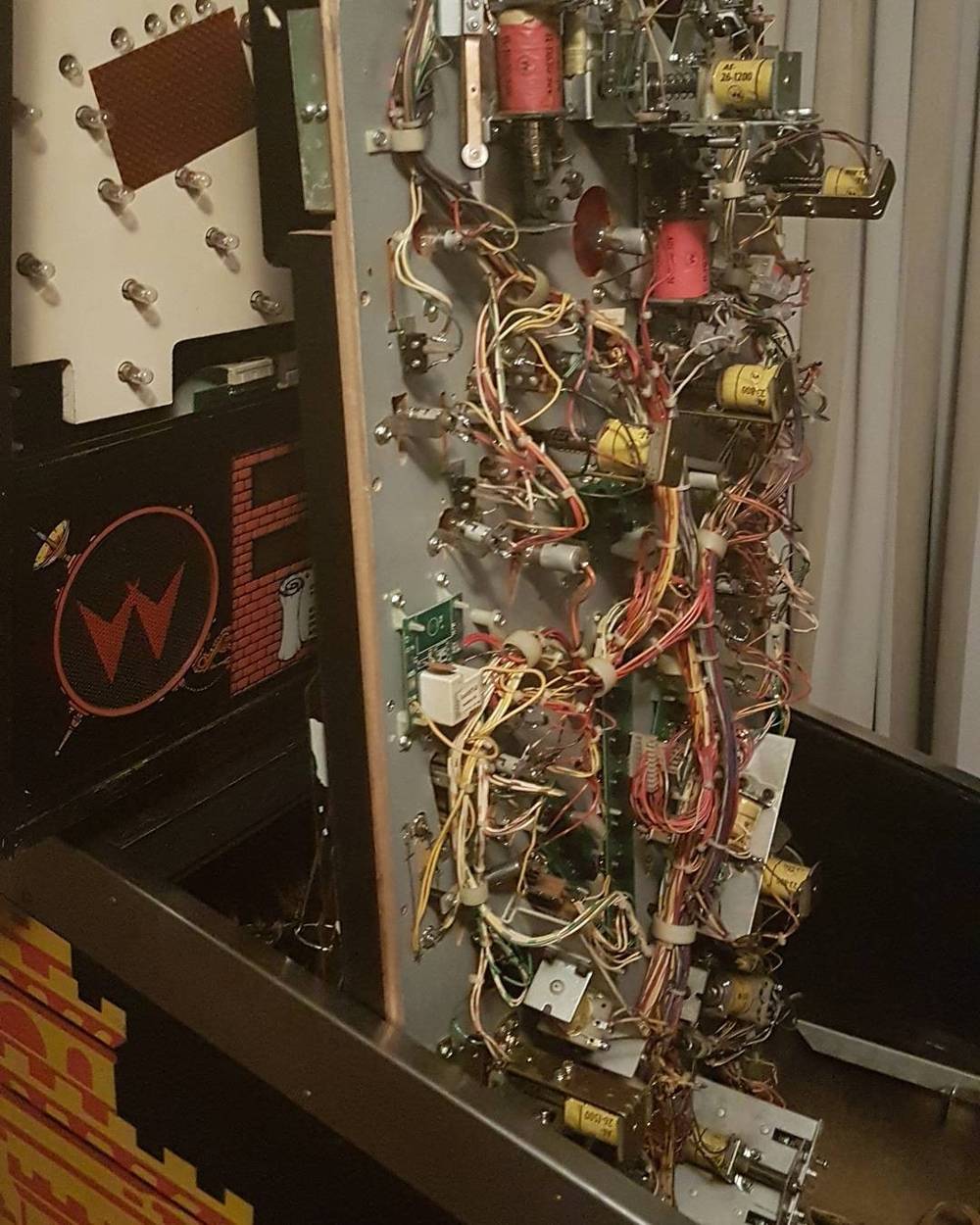 The open back panel of a pinball machine showing its internal wiring and components.