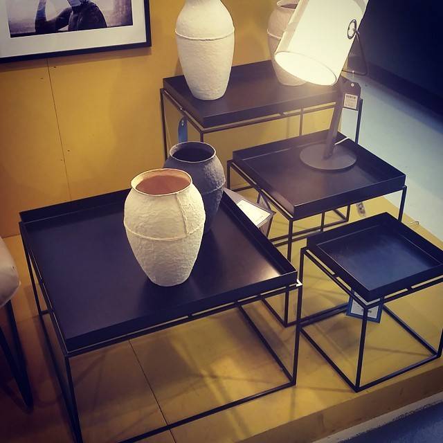 Nesting black side tables displaying ceramic vases and a lamp in a furniture showroom.