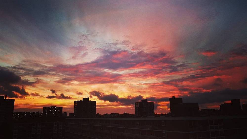 A dramatic red and orange sunset sky over a city skyline silhouette.