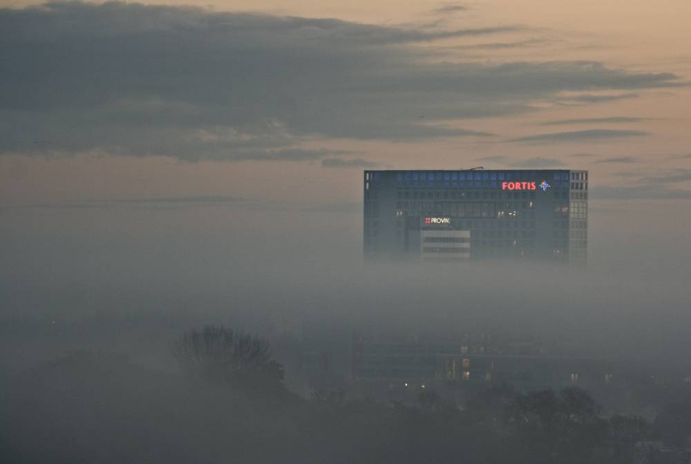The Fortis office tower rising above a thick layer of morning mist, glowing pink at sunrise.