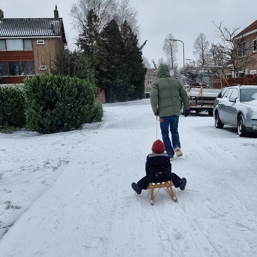 A man pulling a child on a sled along a snow-covered residential street.
