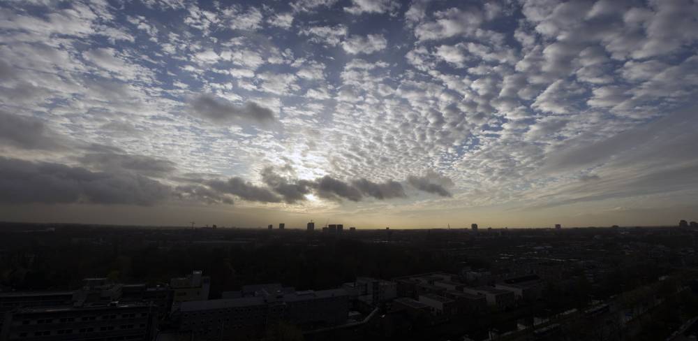 A wide panorama of mottled clouds catching the last light of sunset above the Utrecht skyline.