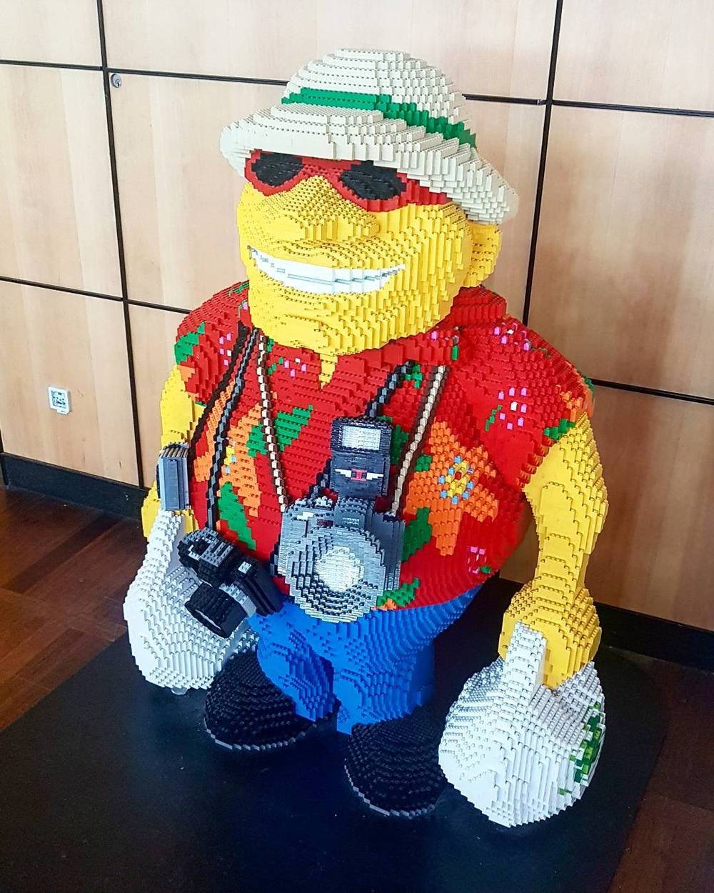 A large Lego figure sculpture dressed as a tourist with a camera, hat, and sunglasses.