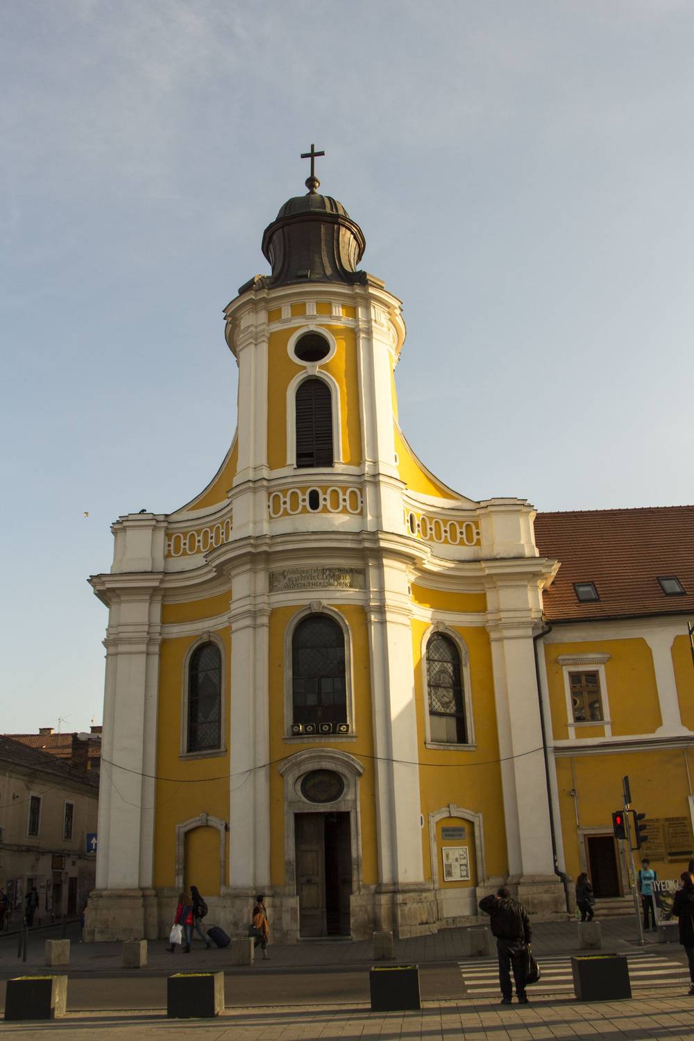 A small yellow baroque church tower on a street corner.