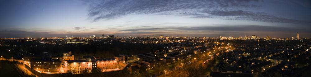 A wide dusk panorama over Utrecht's illuminated streets and rooftops stretching to the horizon.