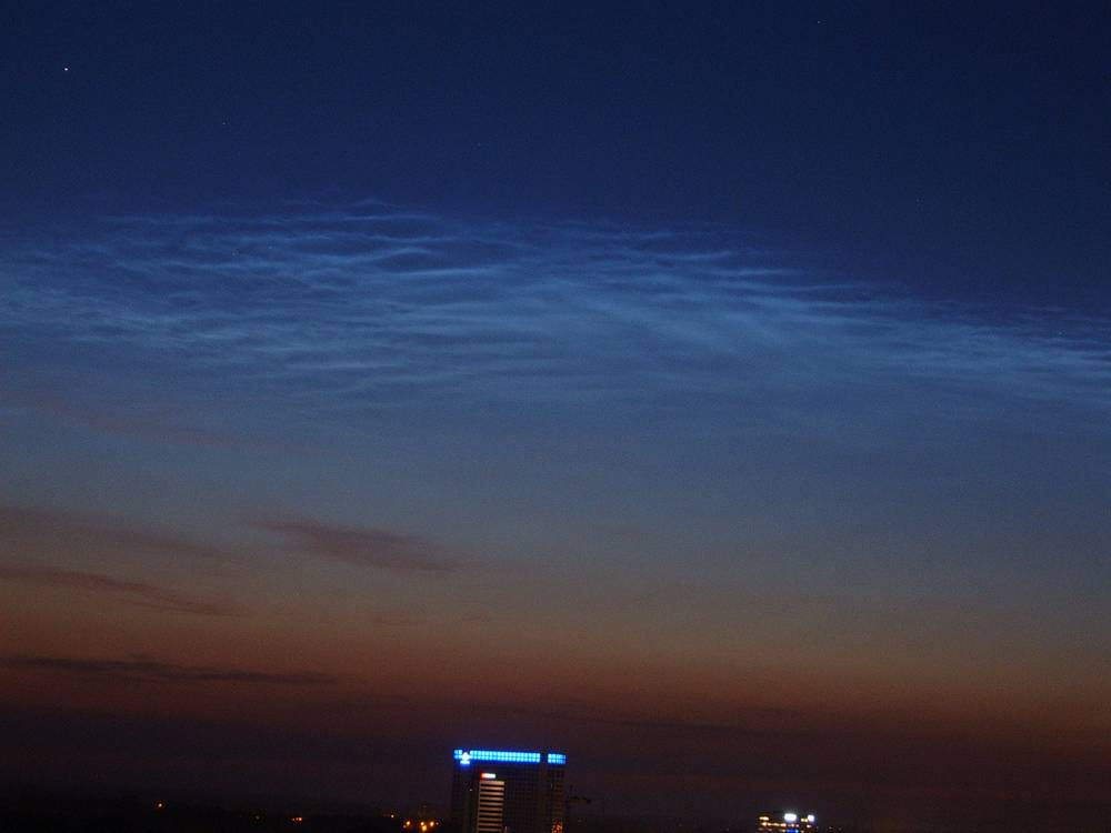 Glowing noctilucent clouds streak across a dark blue night sky above the Utrecht skyline.