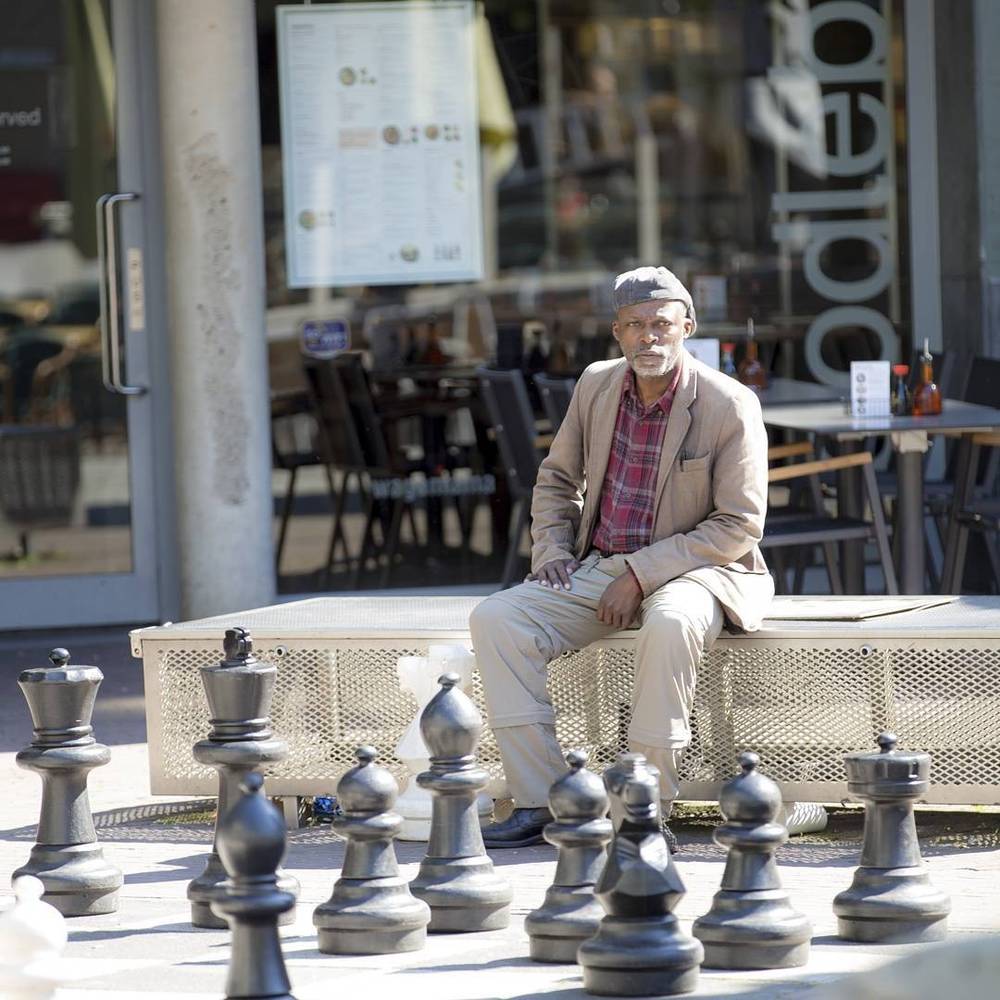 A man sitting on a bench beside an oversized outdoor chess set.