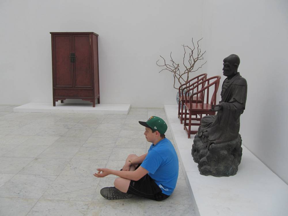 das kind sitzt in einem ausstellungsraum auf der museumsinsel hombroich vor einem sitzenden buddha