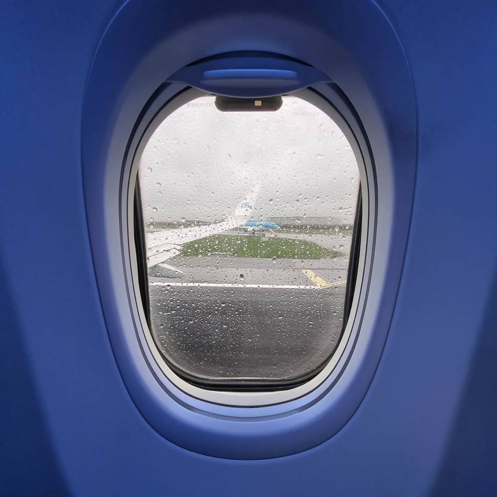 View through a rain-streaked airplane window overlooking a runway and grass field.