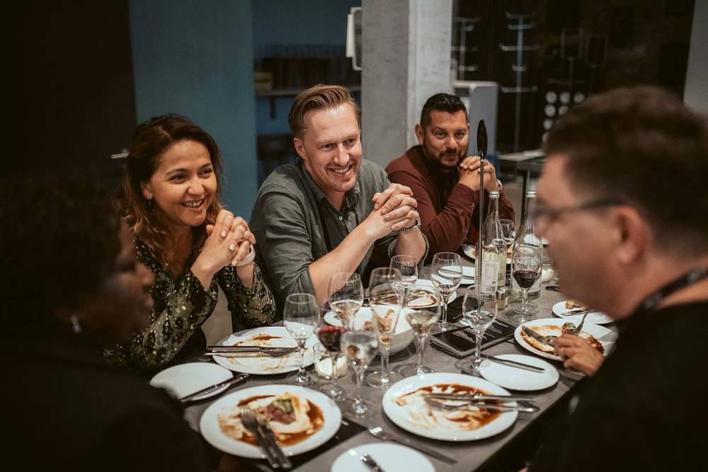 A group of four people clasping hands over a restaurant dinner table.