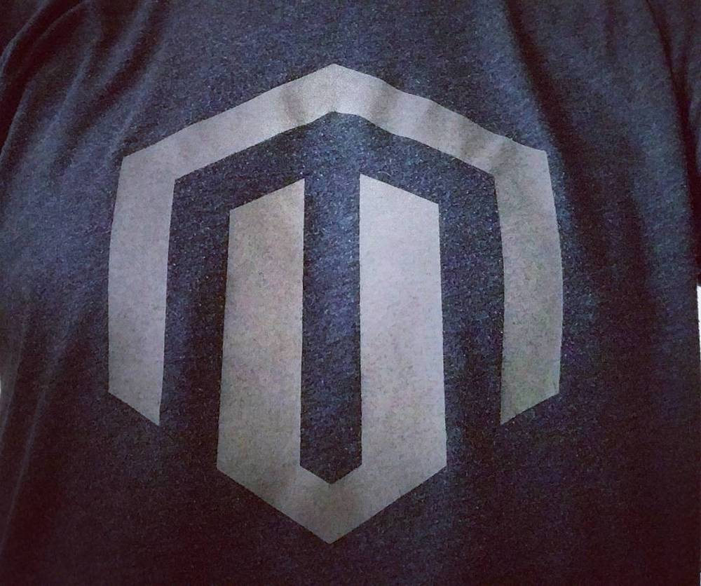 The Magento logo printed on a dark t-shirt.