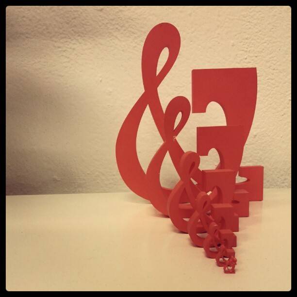 A red sculptural object resembling a stylized musical or graphic symbol on a plinth.