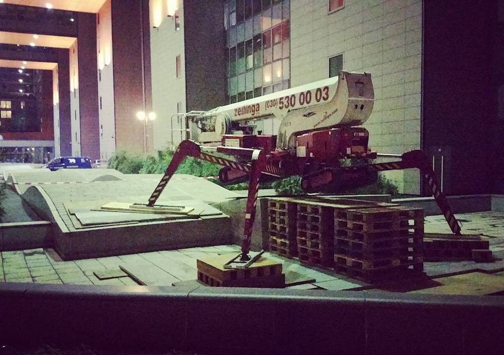 A large boom lift crane parked outside a modern office building at night.