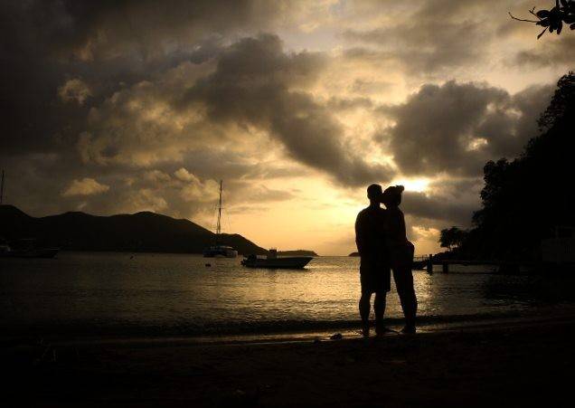 Silhouette of a couple standing together watching a dramatic sunset over the sea.