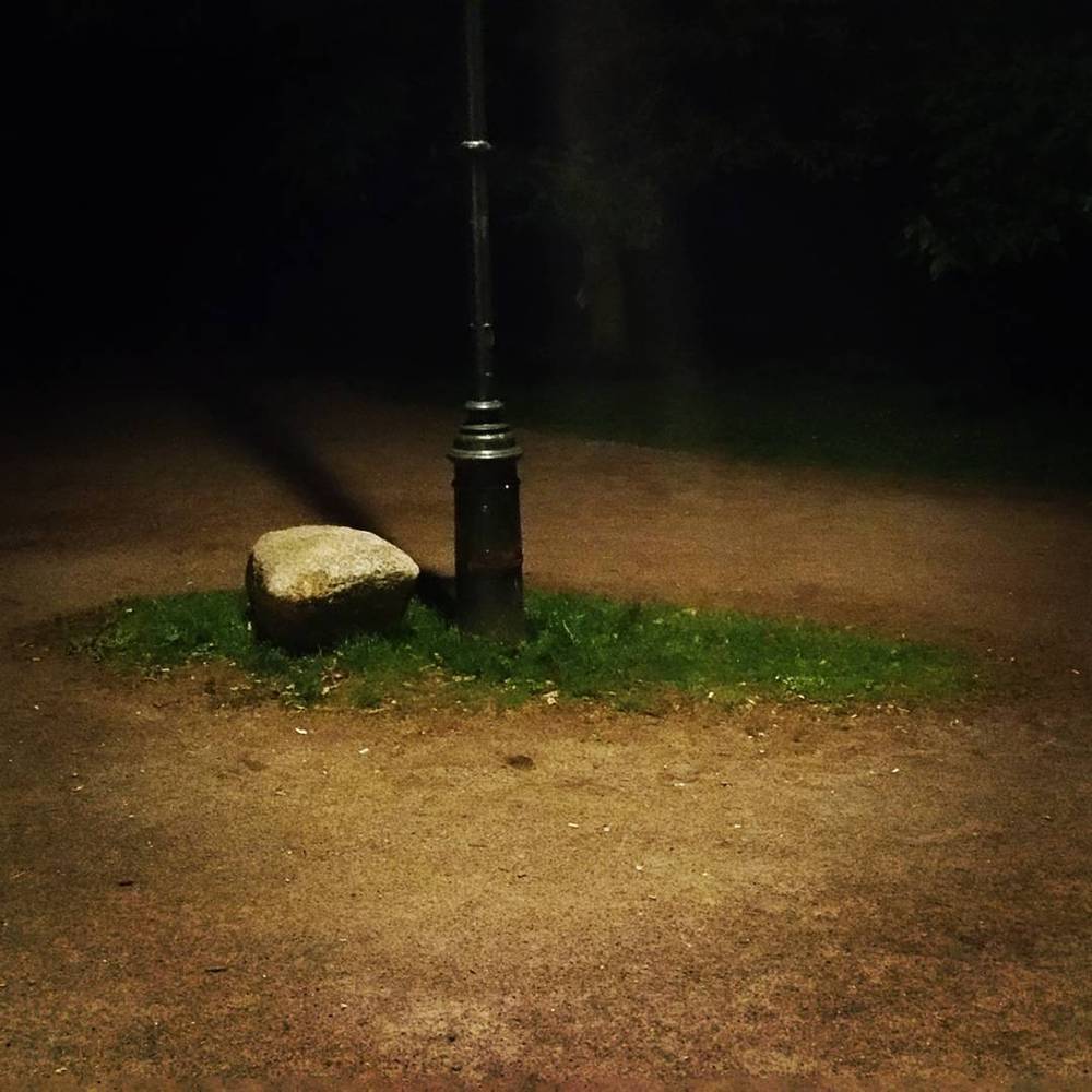 A stone and lamppost forming an improvised roundabout marker on a dirt path at night.