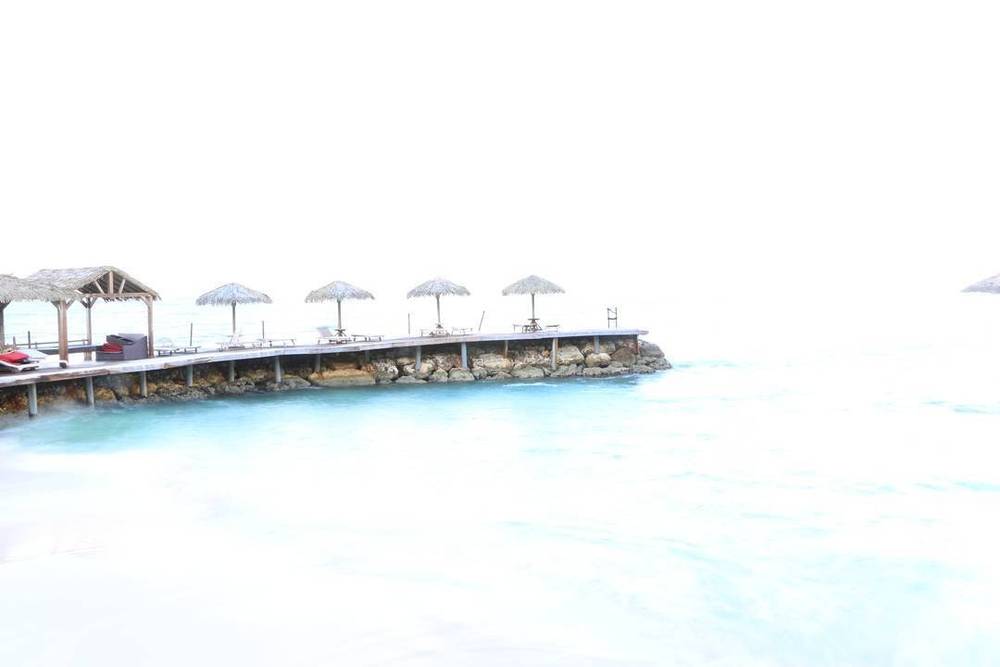 A wooden pier lined with thatched umbrellas extending into turquoise sea.