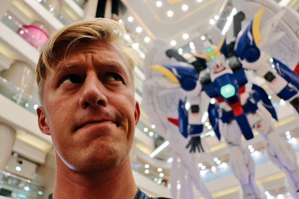A close-up selfie of a man with a giant robot statue looming behind him.