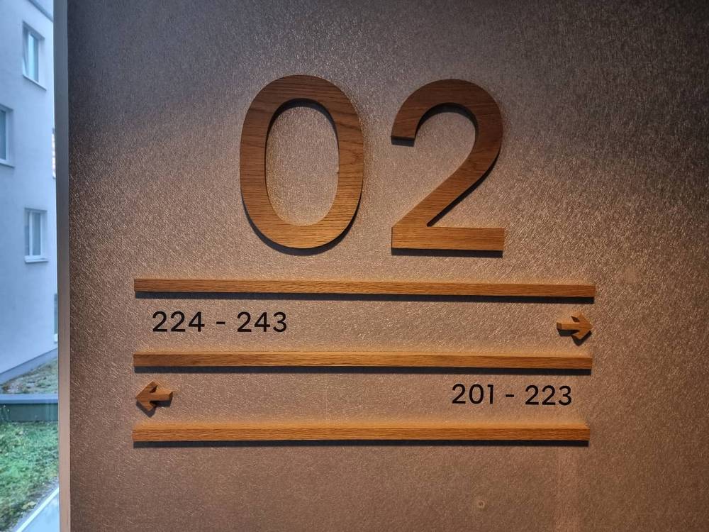 A wooden hotel corridor sign showing directions to room ranges 224 to 243 and 201 to 223.