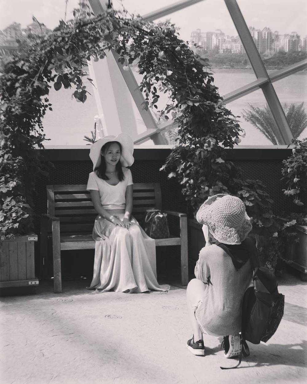 Black and white photo of two people in white outfits under an arched trellis.
