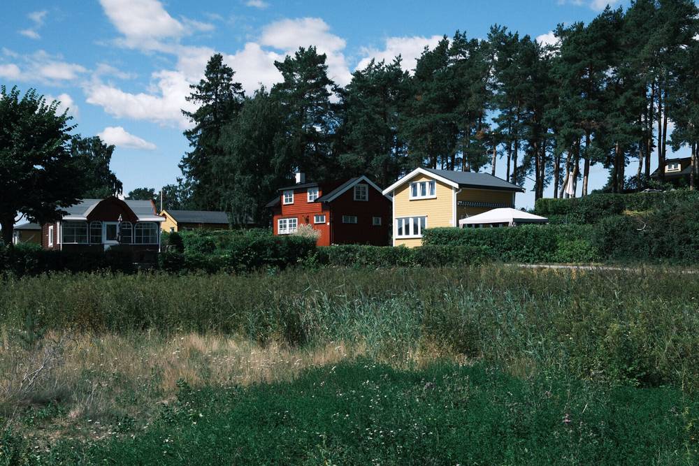 Auto-generated description: A peaceful countryside scene with several houses nestled among tall trees under a blue sky with scattered clouds.