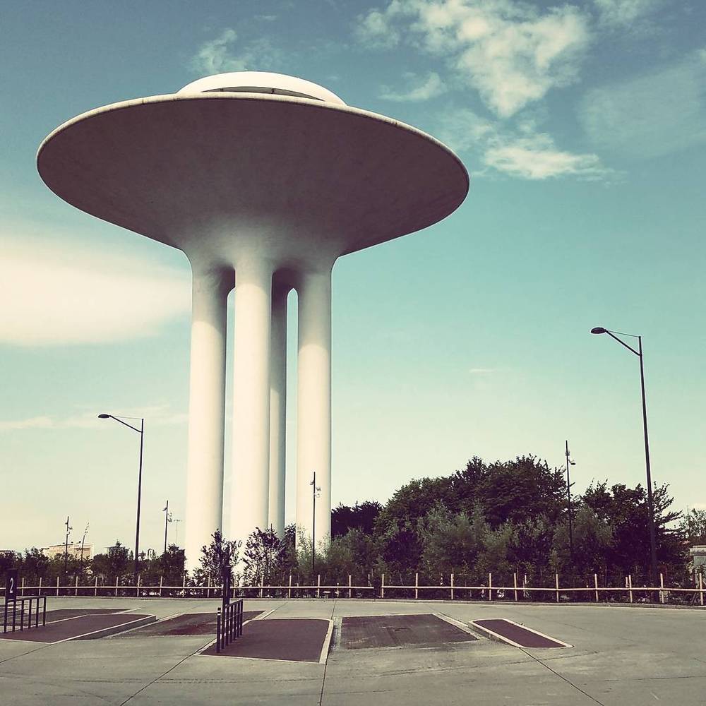 A flying-saucer-shaped water tower on tall concrete pillars against a blue sky.