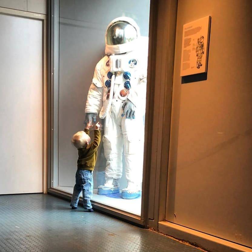 A toddler reaches up to touch an astronaut suit display in a museum.