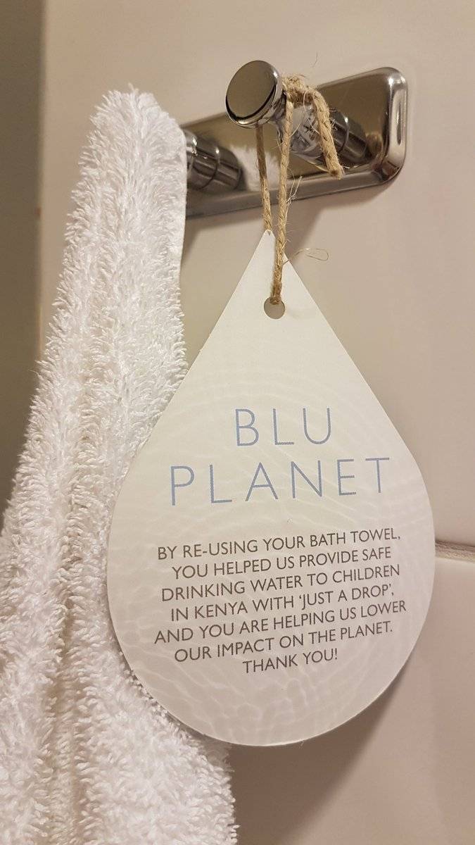 A folded towel hangs with a hotel tag reading "Blu Planet" explaining its towel reuse program.
