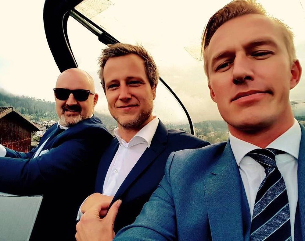 Three men in formal wedding attire pose for a selfie, one wearing sunglasses.