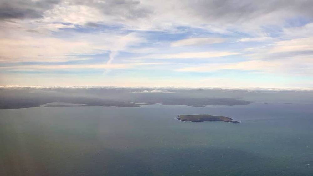 View from an airplane window over the ocean with a small island visible below.