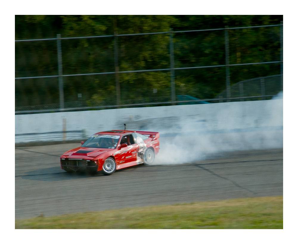 Red 80s Nissan with itasha exiting a corner mid-drift, smoke coming out of the back tires