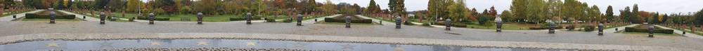 A panoramic view of an open outdoor memorial park with low stone structures and autumn trees.
