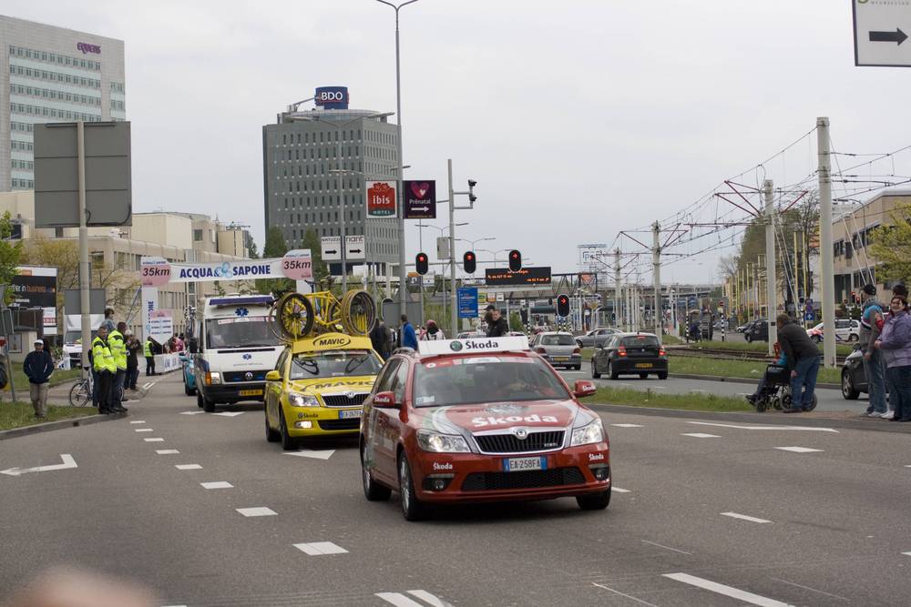 A yellow Mavic neutral support car with spare wheels on the roof follows the race.
