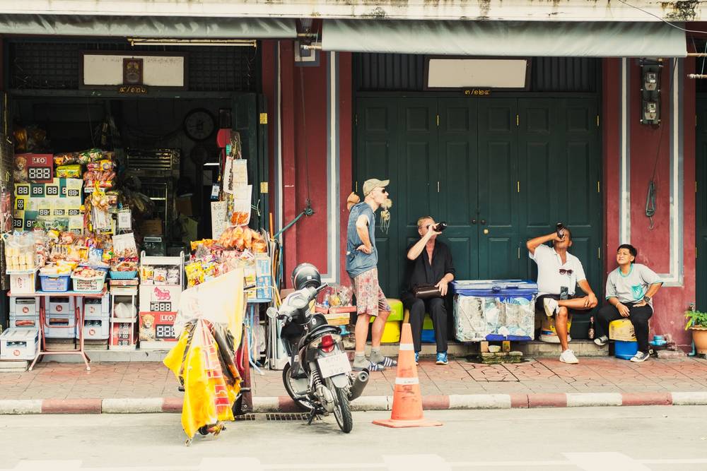 Men sitting by the road enjoying some beer on a warm sunny afternoon next to a small grocery store