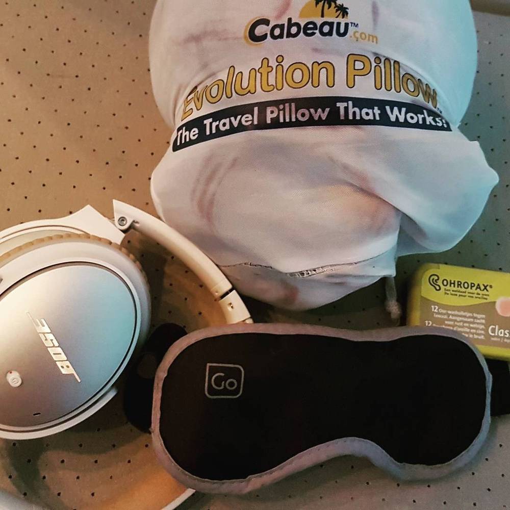 Travel accessories including a neck pillow, headphones, earplugs, and a sleep mask on a table.