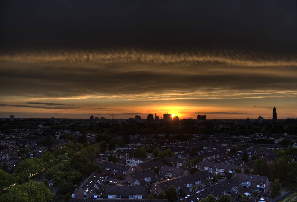 A wide sunset over the Utrecht skyline seen from a rooftop, with rows of houses in the foreground and church towers on the horizon.