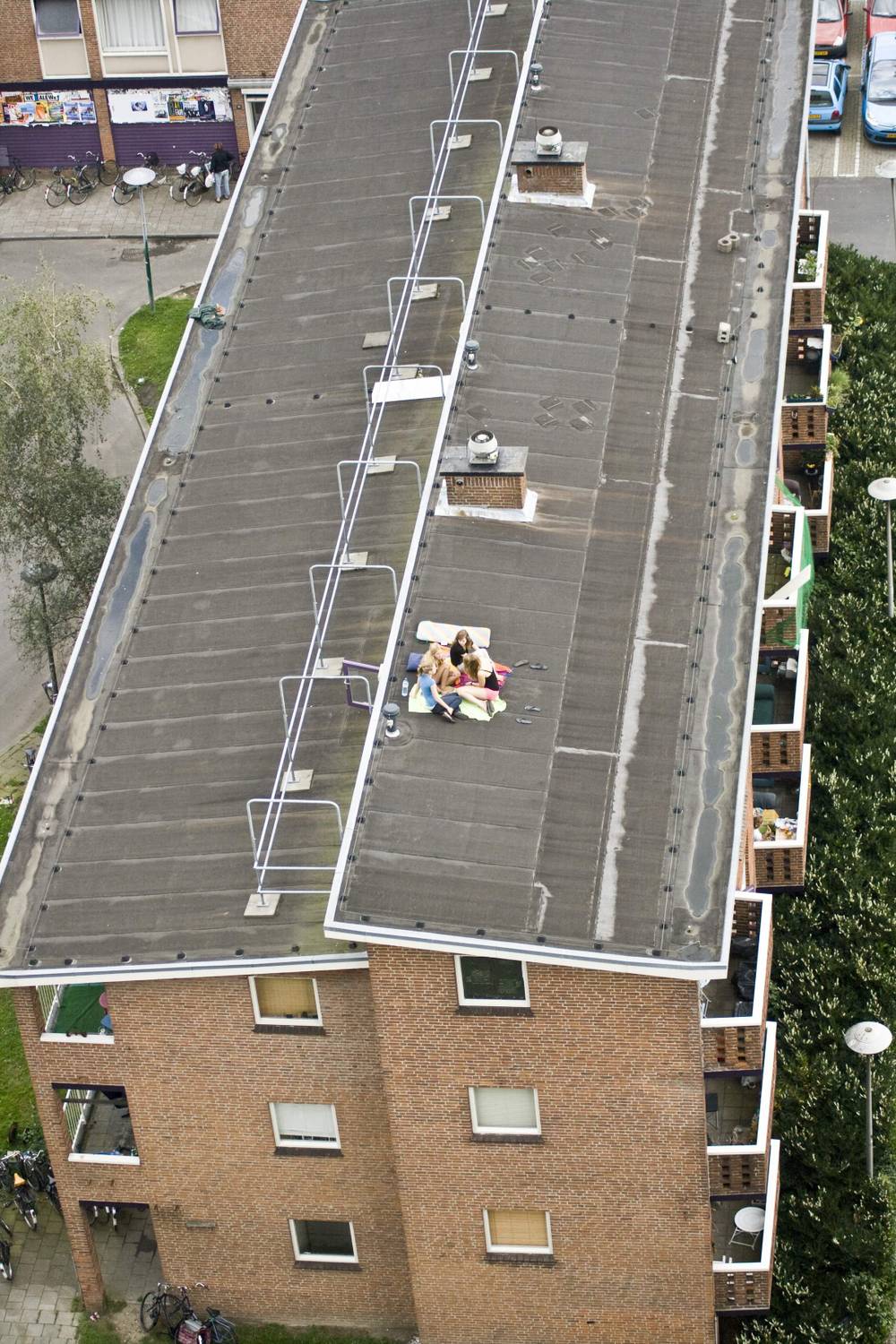 An aerial view straight down onto a flat rooftop with solar panels, where two people sit sunbathing.