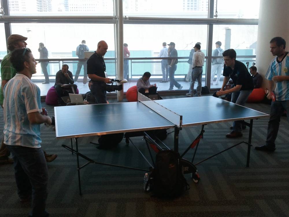 Conference attendees play table tennis in a lounge near floor-to-ceiling windows.