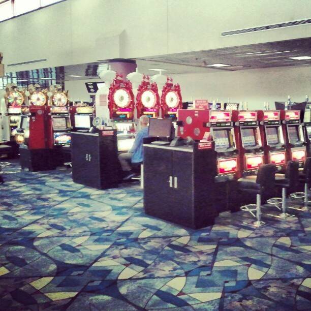 Rows of slot machines on a patterned carpet inside an airport gaming lounge.