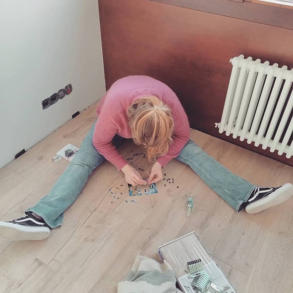 A person assembling a jigsaw puzzle on the floor next to a radiator.