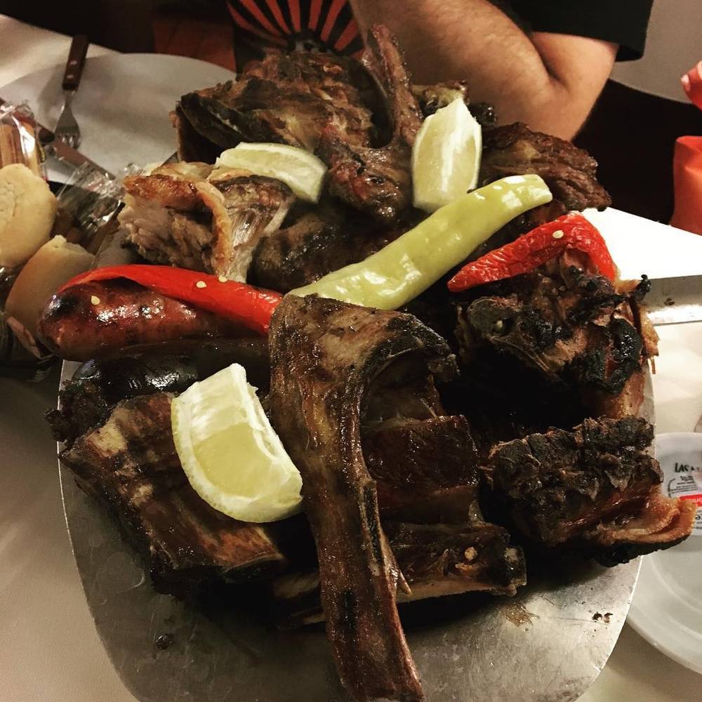 A plate of grilled ribs and sausages garnished with lemon wedges.
