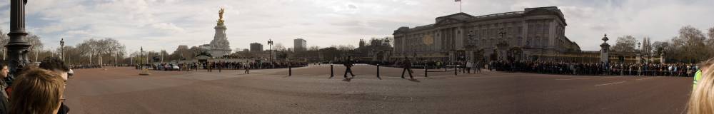 A panoramic view of Buckingham Palace with guards lined up before a crowd.