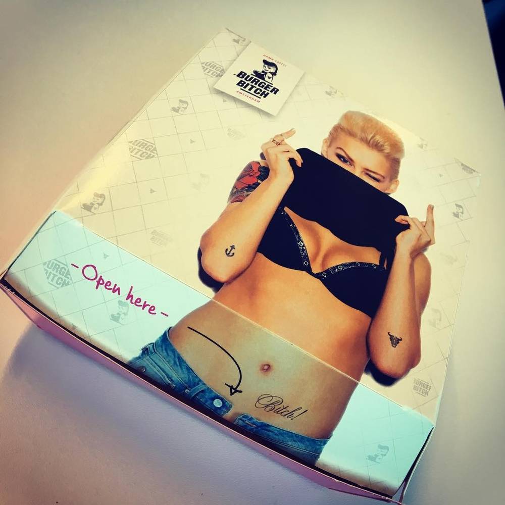 A takeaway box for Burger Bitch printed with a pin-up style illustration and the text "Open here".