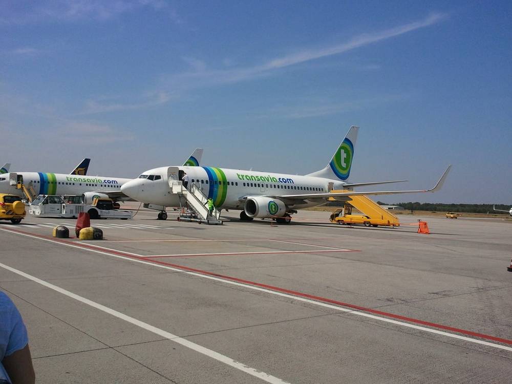 A Transavia airplane sits parked at the gate under a clear blue sky.