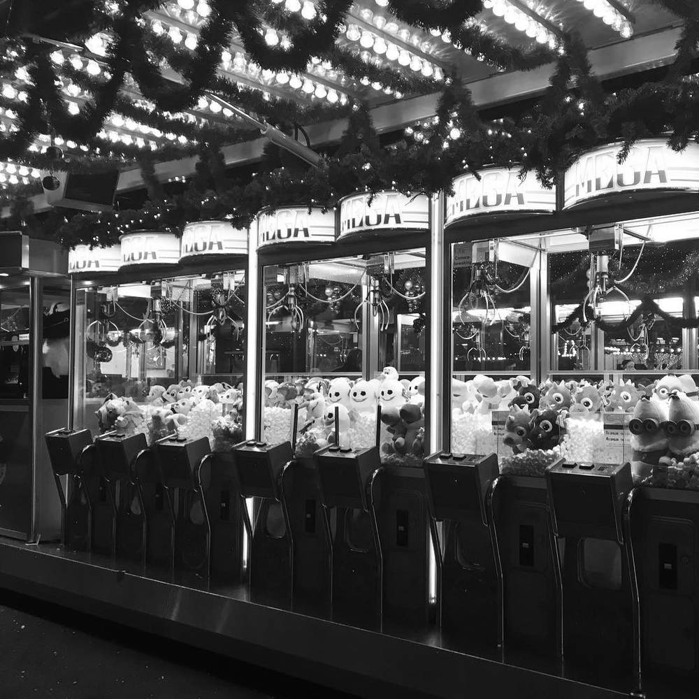 A black and white photo of an arcade claw machine game at a fairground.